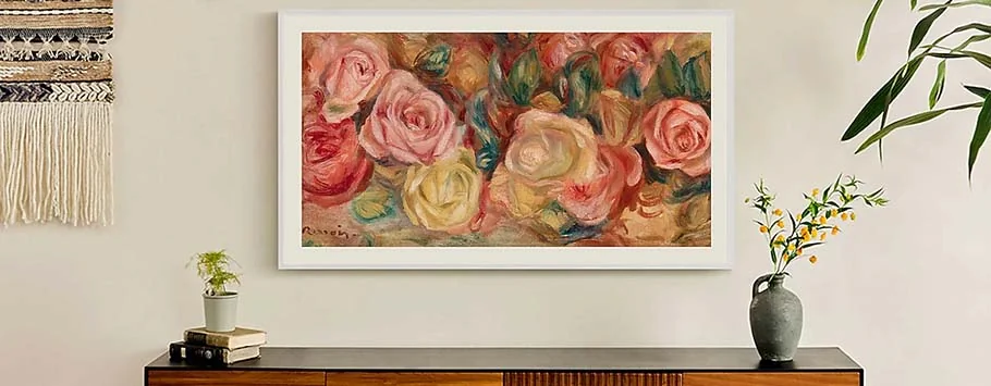 Framed painting of vibrant roses in red, pink, and yellow hues on a beige wall. Below, a wooden table with potted plants adds a serene touch.