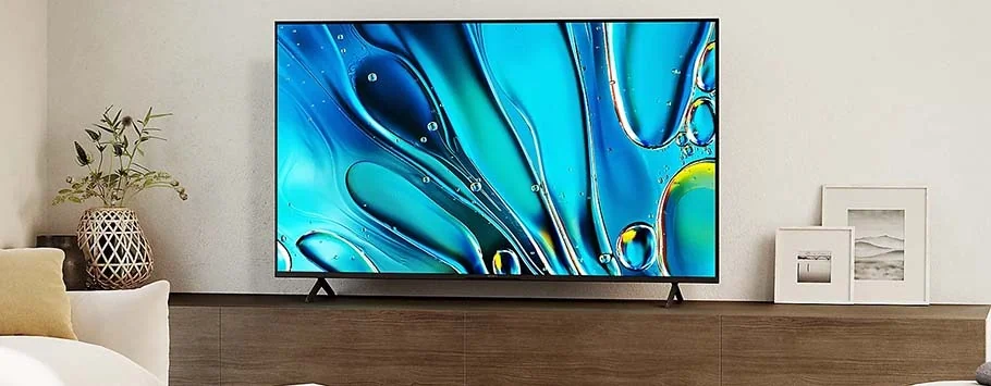 A modern living room with a sleek, wall-mounted flat-screen TV displaying abstract blue and yellow swirls. A potted plant and framed photos add décor.