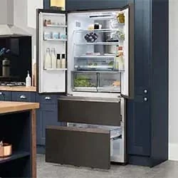 A sleek, open stainless steel refrigerator in a modern kitchen with navy cabinets. It shows organized shelves with drinks, containers, and fresh produce.