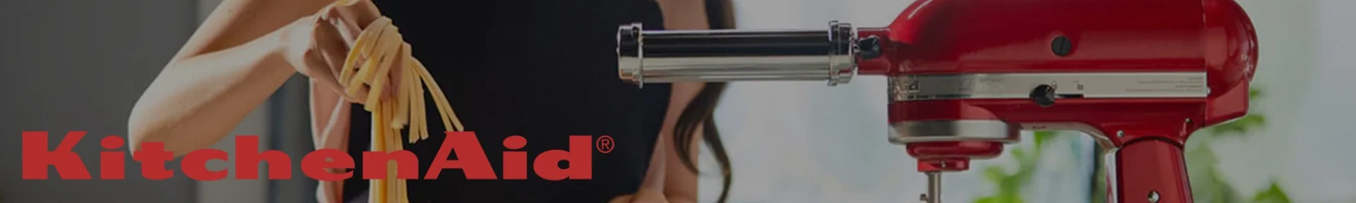 A person in a kitchen pulls fresh pasta from a red KitchenAid mixer with an attachment.