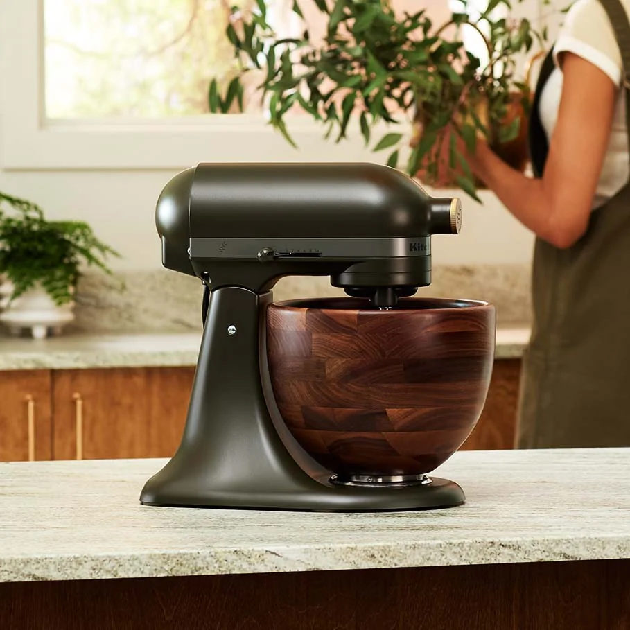 A sleek black stand mixer with a large wooden bowl sits on a kitchen countertop.