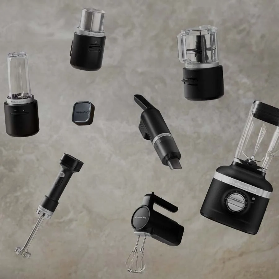 Floating against a textured grey background are various black KitchenAid appliances, including blenders, mixers, and an immersion blender.
