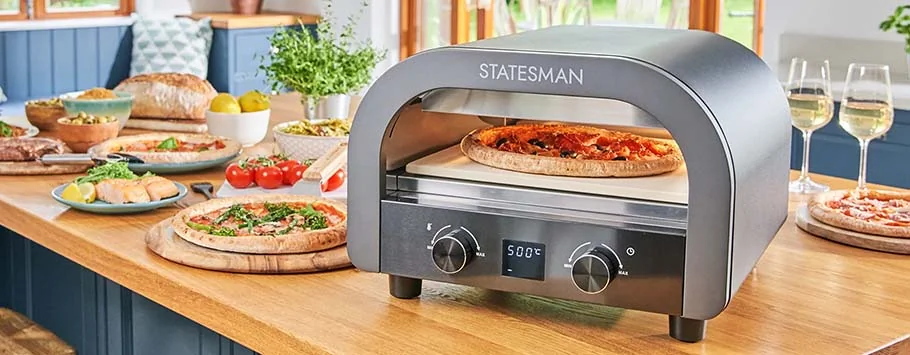 Pizza oven on a wooden counter with a fresh pizza inside. Surrounding the oven are various dishes, salad bowls, and glasses of white wine, evoking a cosy dining atmosphere.