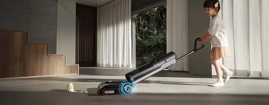 A young girl joyfully pushes a sleek, modern vacuum cleaner over a tiled floor. Sunlight filters through curtains, creating a warm and tidy atmosphere.
