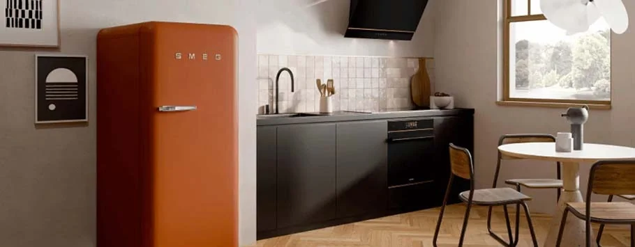 A modern kitchen with a retro orange fridge stands on the left. Black cabinets and counters are in the centre, and a round table with chairs is by the window, creating a warm and cosy ambiance.