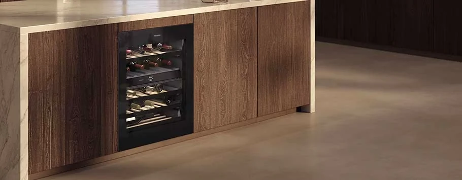 Modern kitchen with light wood cabinetry, featuring a built-in glass-front wine cooler stocked with wine bottles. Warm and sophisticated ambiance.