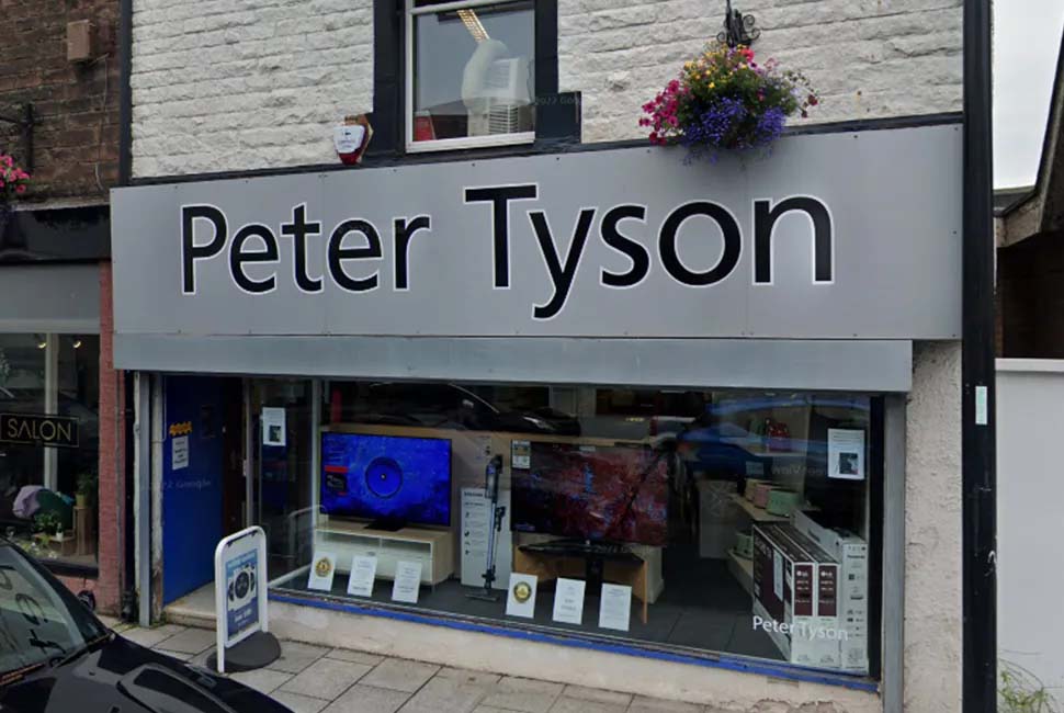 Storefront of "Peter Tyson" with modern electronics displayed in the window, including TVs and audio equipment. Outside, a hanging basket of flowers adds color.