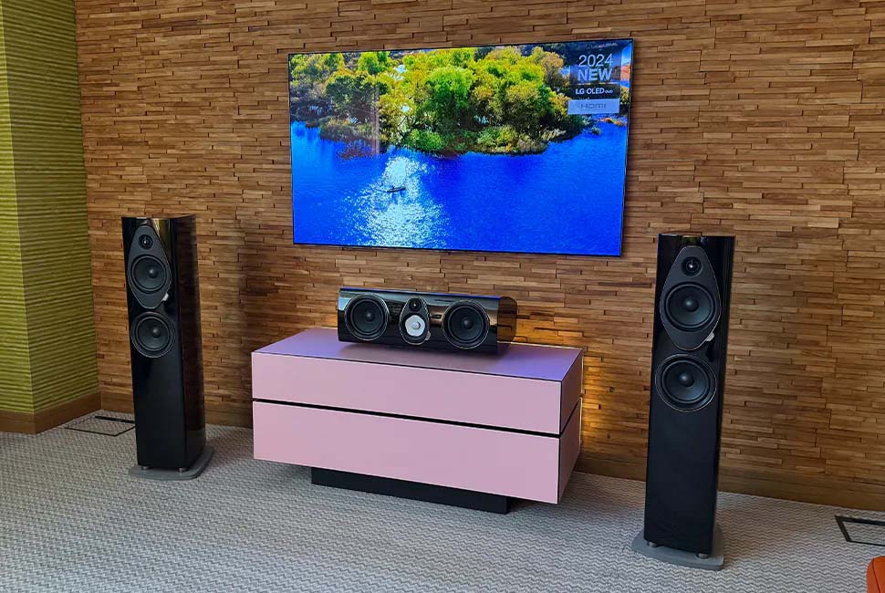 Modern living room setup with a large flat-screen TV displaying a vibrant nature scene. Flanked by tall black speakers, a pink TV stand sits below.