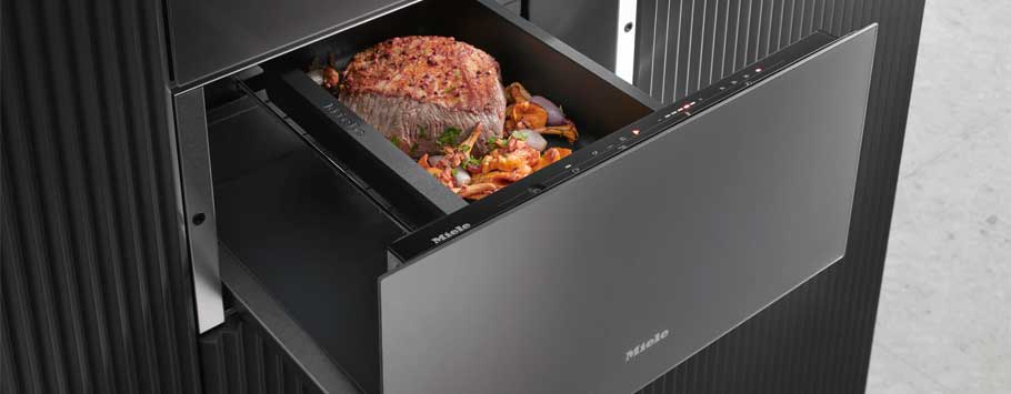 Modern oven drawer slightly open, revealing a seasoned roast surrounded by chopped vegetables. Sleek black design conveys a contemporary, sophisticated feel.