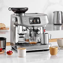 Modern stainless steel espresso machine on a kitchen counter with a digital display. Surrounded by filled coffee cups and kitchen items, conveying a cozy, inviting atmosphere.