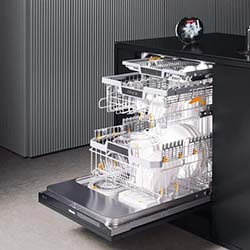 Open dishwasher in a modern kitchen, filled with white dishes and utensils. The sleek dark cabinets and minimalist decor create a clean, organized look.