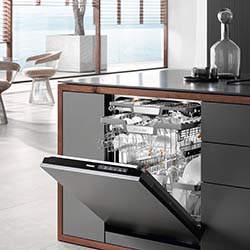 Modern kitchen with an open dishwasher showing neatly arranged dishes and glasses. Sleek design, minimalistic decor, large windows provide natural light.