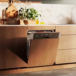 Open wooden cabinet dishwasher in a modern kitchen with plants and utensils on the marble countertop, conveying a warm and sleek ambiance.