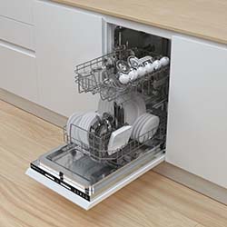 Open dishwasher in a modern kitchen with wooden flooring. It is fully loaded with white dishes, bowls, and cups, neatly arranged on both racks.