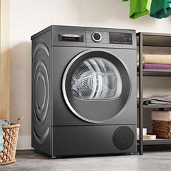 Modern black front-load washing machine in a laundry room. Shelves with towels are in the background, and a woven basket is placed nearby on the floor.