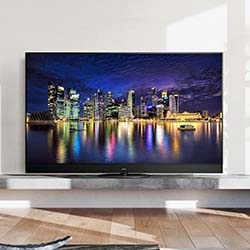 A flat-screen TV on a wooden stand displays a vibrant cityscape at night. Skyscrapers reflect colorful lights on the water, creating a lively and modern atmosphere.