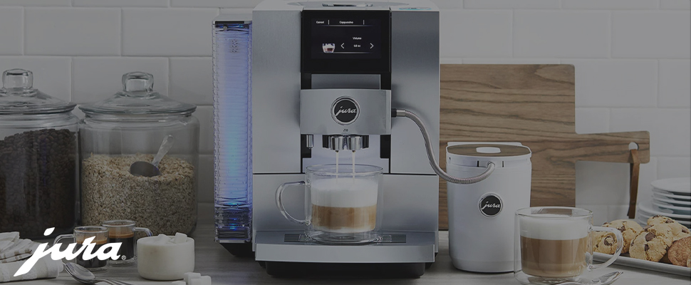 Coffee station with espresso machine preparing a cappuccino in a glass mug. Nearby are jars of coffee beans, an oat container, and a plate of cookies.