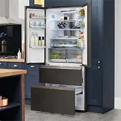 A sleek, open stainless steel refrigerator in a modern kitchen with navy cabinets. It shows organized shelves with drinks, containers, and fresh produce.