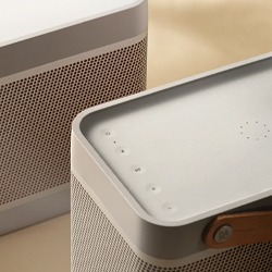 Close-up of two sleek, minimalist speakers with light grey tones and perforated metal grills, conveying a modern and sophisticated design.