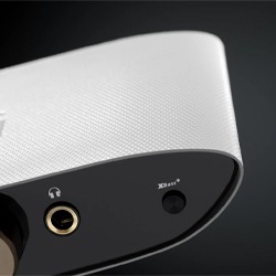 Close-up of a sleek, white, and black electronic device against a dark background. It features a headphone jack and button, conveying a modern, minimalist design.