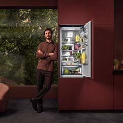 Cream-colored coffee maker brewing fresh coffee, next to a plate of granola squares on a light-coloured countertop.