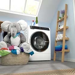 Stuffed elephant in laundry basket with colorful towels beside a washing machine. Ladder shelf with rolled towels and decor creates a cozy, organized vibe.