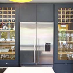 Modern kitchen with a stainless steel double-door fridge, flanked by glass cabinets displaying wine glasses and dishware, creating a sleek, organized look.
