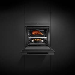 Modern black oven in sleek kitchen, door open. Inside, a roast chicken on top rack and vegetables on bottom tray, creating a warm, inviting cooking scene.