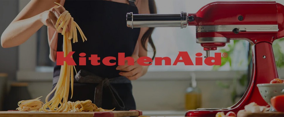 A person in a kitchen pulls fresh pasta from a red KitchenAid mixer with an attachment.