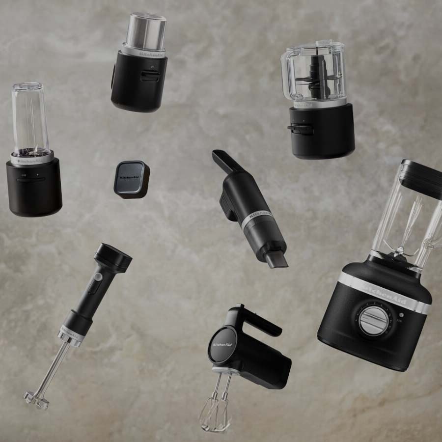 Floating against a textured grey background are various black KitchenAid appliances, including blenders, mixers, and an immersion blender.