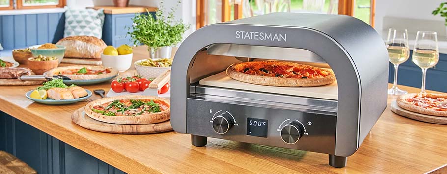 Pizza oven on a wooden counter with a fresh pizza inside. Surrounding the oven are various dishes, salad bowls, and glasses of white wine, evoking a cosy dining atmosphere.
