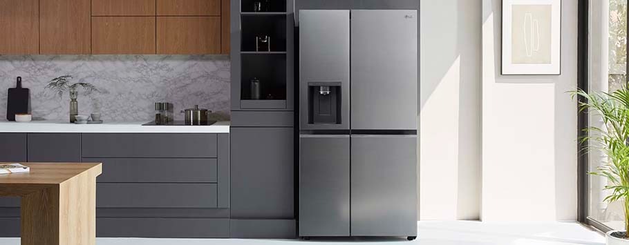 Modern kitchen with a sleek grey refrigerator, marble backsplash, and wooden cabinets. Sunlit space features minimalist decor and a potted plant.