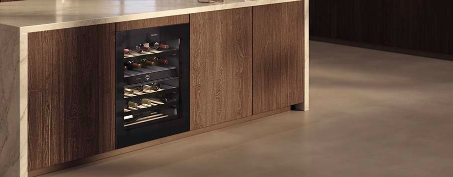 Modern kitchen with light wood cabinetry, featuring a built-in glass-front wine cooler stocked with wine bottles. Warm and sophisticated ambiance.