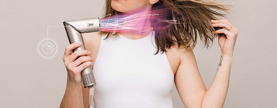 A woman in a white tank top uses a high-tech hair dryer emitting colorful airflow on her hair. She appears satisfied, conveying efficient hair styling.