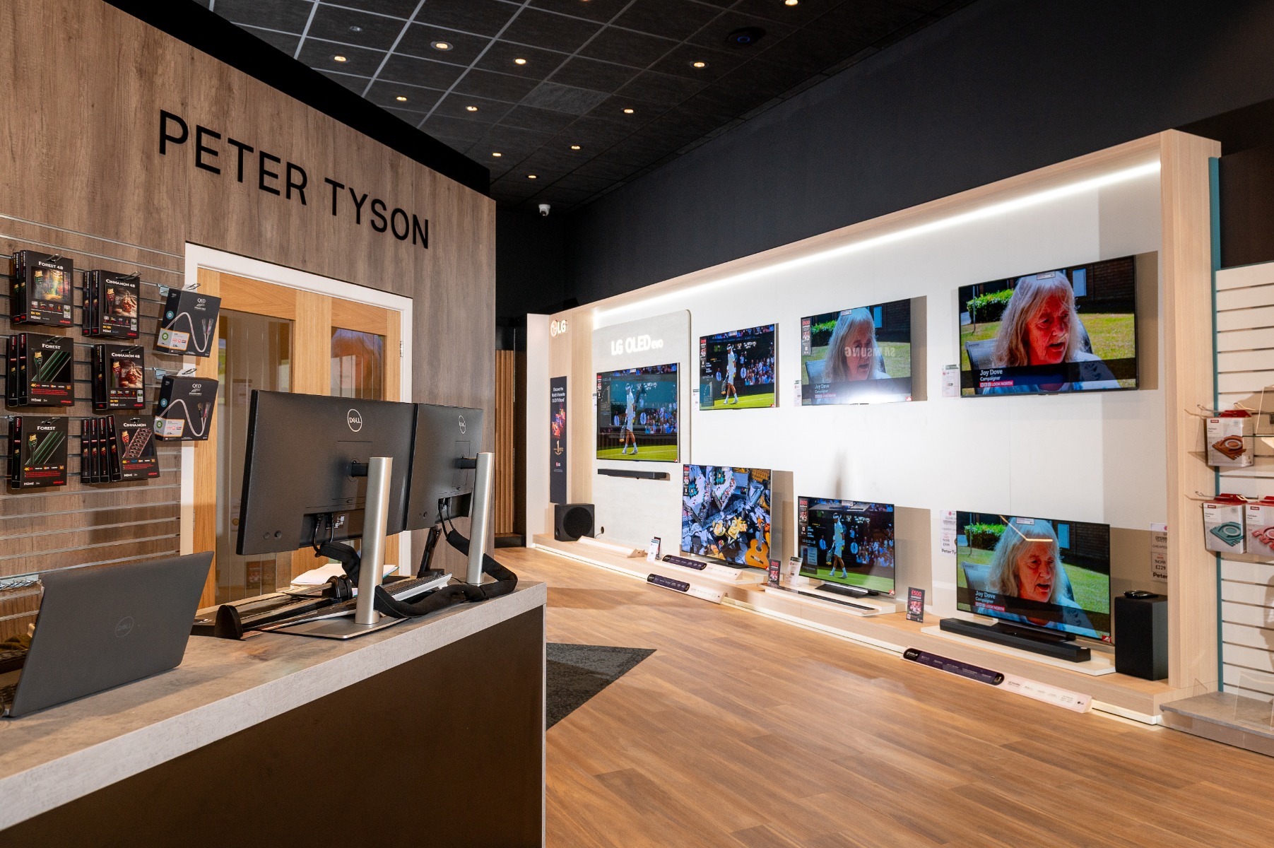Store interior with "Peter Tyson" sign, featuring a display of mounted TVs, some showing sports and others a woman speaking. 